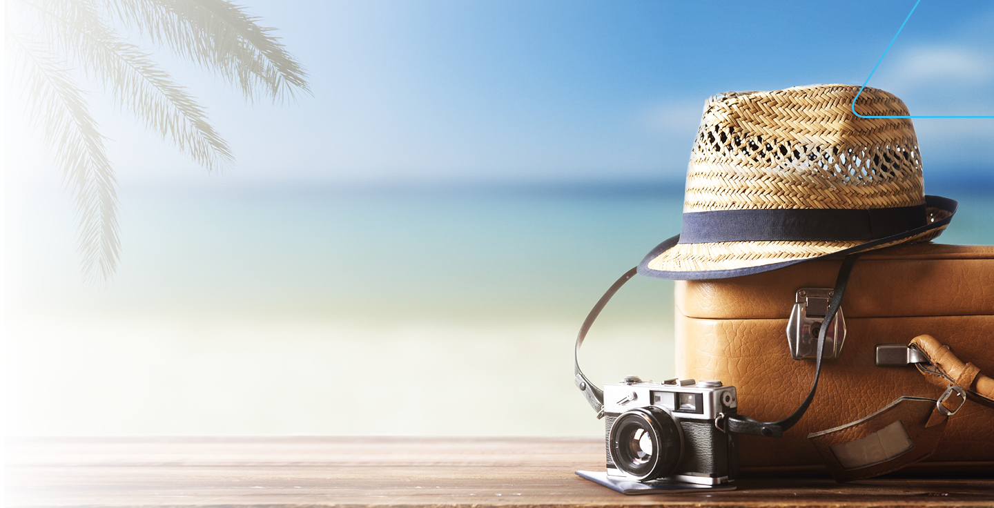 Foto de uma câmera fotográfica, uma mala de viagens e um chapéu com a praia ao fundo.